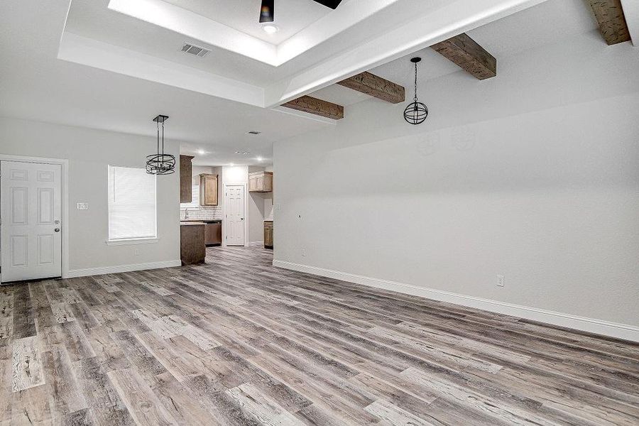 Unfurnished living room featuring beamed ceiling, wood-type flooring, and a raised ceiling