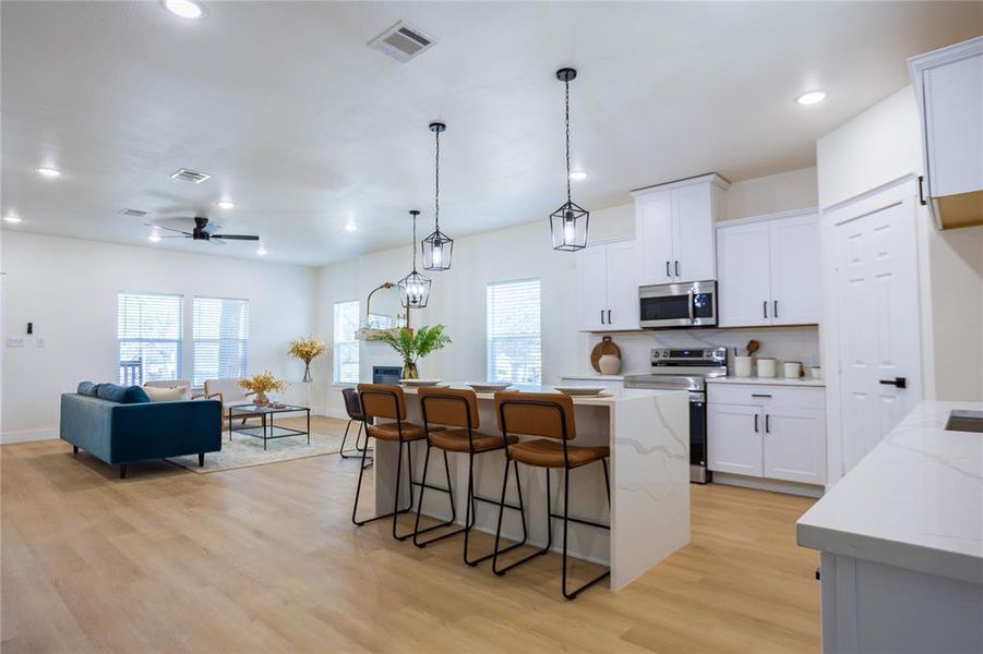Kitchen featuring a kitchen island, hanging light fixtures, light stone countertops, a kitchen bar, and stainless steel appliances