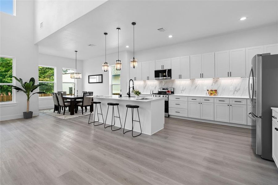 Kitchen with white cabinets, a breakfast bar area, backsplash, appliances with stainless steel finishes, and a kitchen island with sink Kitchen with white cabinets, a breakfast bar area, backsplash, appliances with stainless steel finishes, and a kitchen island with sink