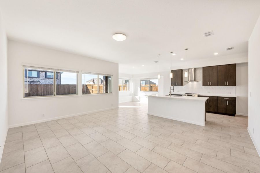 Open-concept living area and kitchen with white island, dark cabinets, tile floors, and pendant lights
