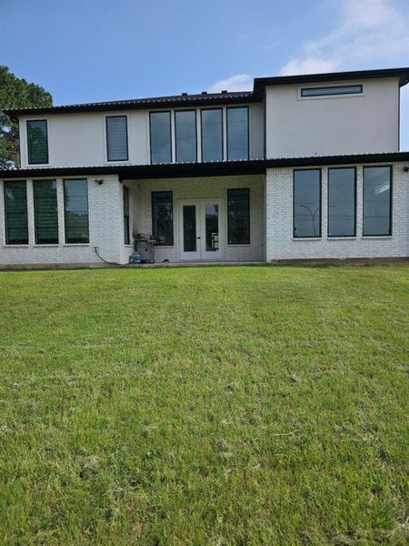 Back of house with a lawn, brick siding, a patio, and stucco siding