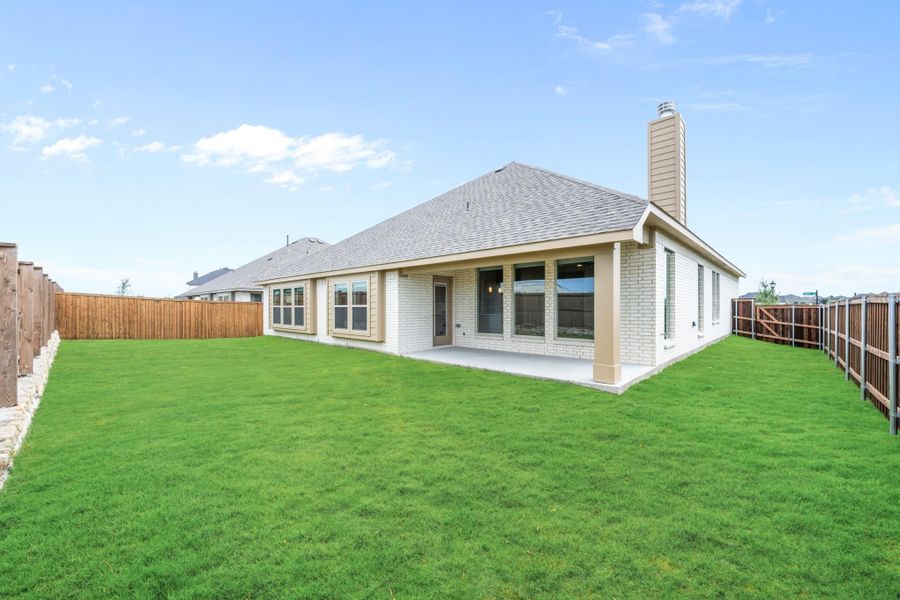 Rear view of single-story brick home with covered patio, chimney, and fenced backyard with green lawn