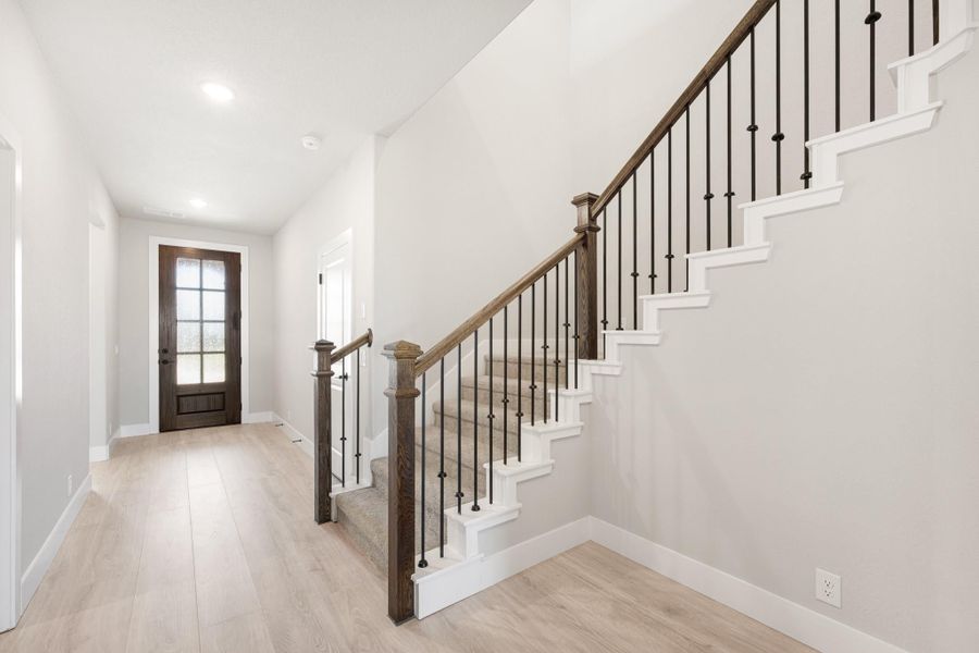 Entryway with staircase featuring wood handrail, black iron balusters, and light hardwood floors leading to front door. Entryway with staircase featuring wood handrail, black iron balusters, and light hardwood floors leading to front door.