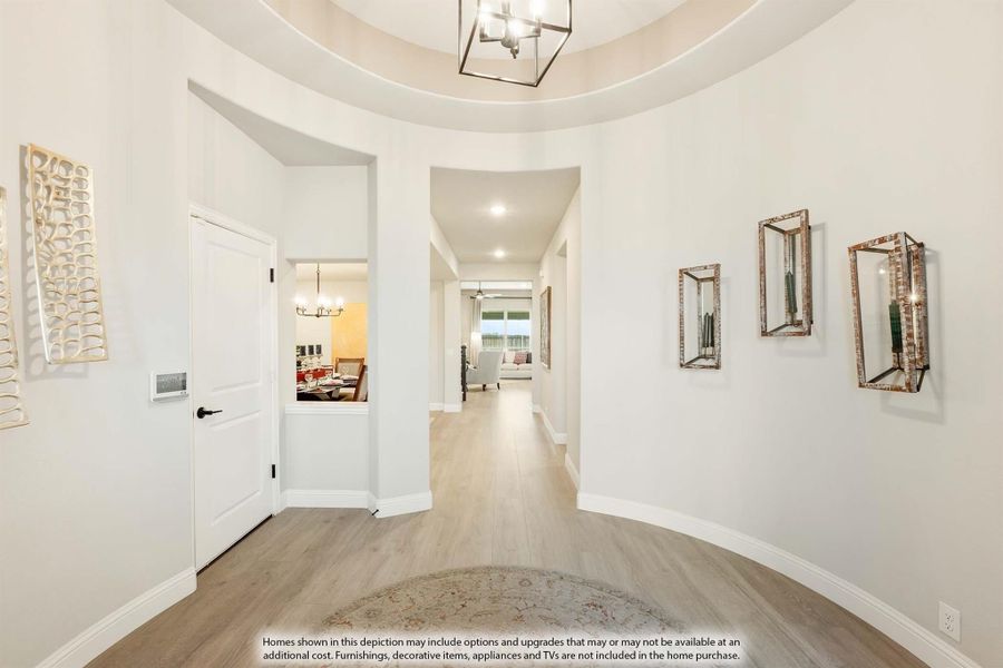 Curved foyer with tray ceiling, pendant light, hardwood floors, and hallway leading to living areas Curved foyer with tray ceiling, pendant light, hardwood floors, and hallway leading to living areas