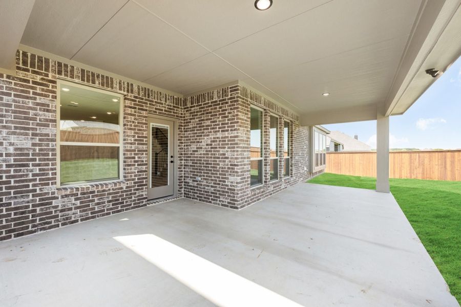 Covered back patio with concrete floor, brick exterior, and fenced backyard with green lawn