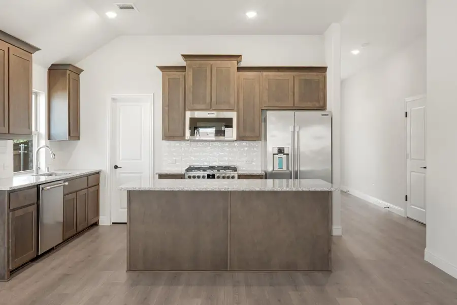 Kitchen with brown wood cabinets, granite island, stainless steel appliances, and light hardwood floors Kitchen with brown wood cabinets, granite island, stainless steel appliances, and light hardwood floors