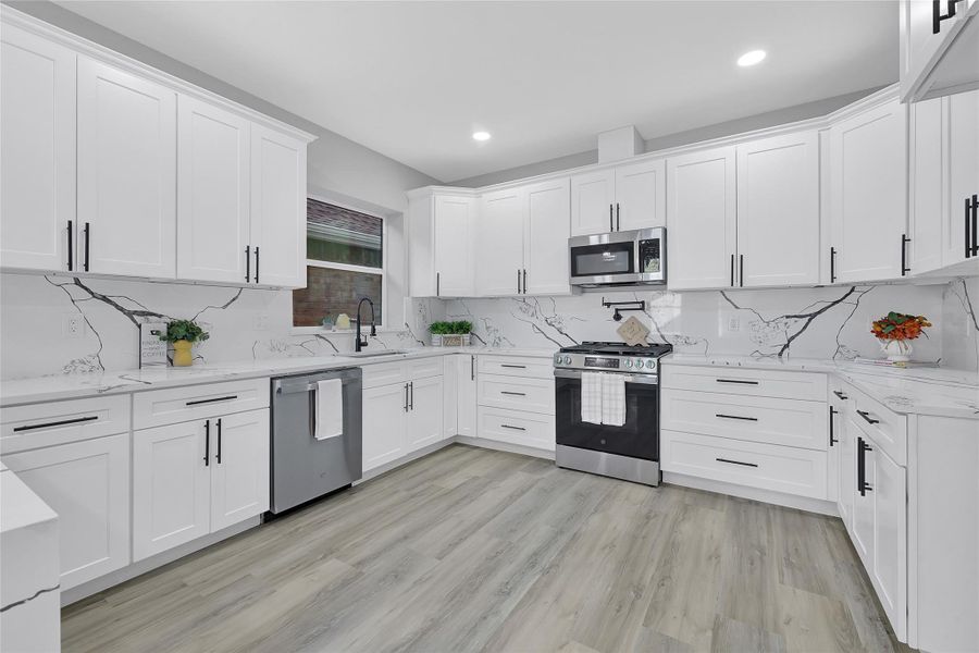 This modern kitchen features sleek white cabinetry, a stylish marble-patterned backsplash, and stainless steel appliances. The spacious layout and wood-style flooring create a bright, inviting atmosphere ideal for cooking and entertaining.