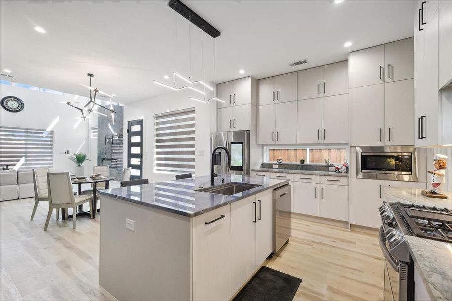 Kitchen with appliances with stainless steel finishes, sink, hanging light fixtures, light wood-type flooring, and an island with sink