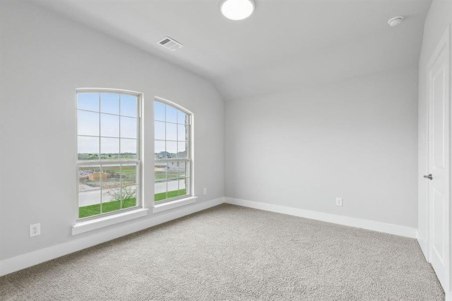 Carpeted spare room featuring vaulted ceiling, healthy amount of natural light, and a smoke detector Carpeted spare room featuring vaulted ceiling, healthy amount of natural light, and a smoke detector
