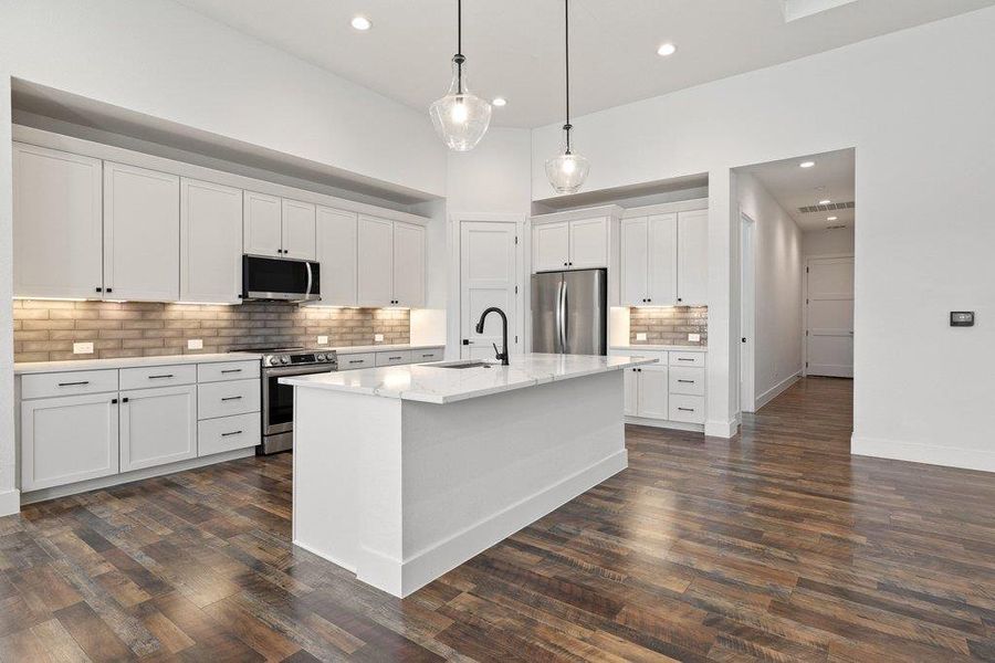 Kitchen featuring white cabinets, backsplash, stainless steel appliances, a kitchen island with sink, and light stone counters