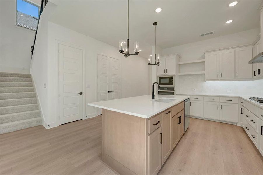 Modern kitchen featuring a central island with a sink, white shaker cabinetry, stainless steel appliances, light wood-finish flooring, and recessed lighting Modern kitchen featuring a central island with a sink, white shaker cabinetry, stainless steel appliances, light wood-finish flooring, and recessed lighting