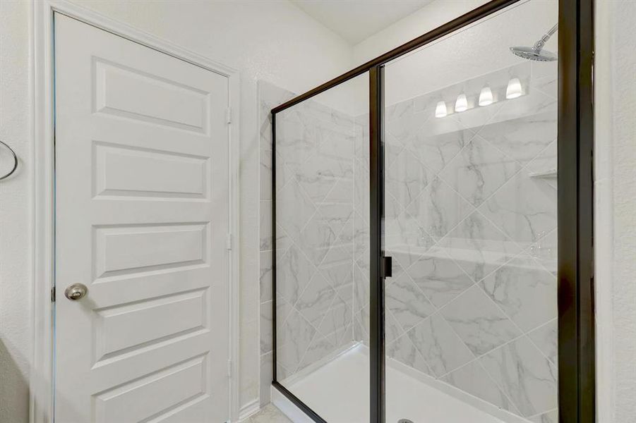 Warm and inviting bathroom with a stylish black-framed shower adorned with elegant marble tile, blending comfort with timeless luxury.