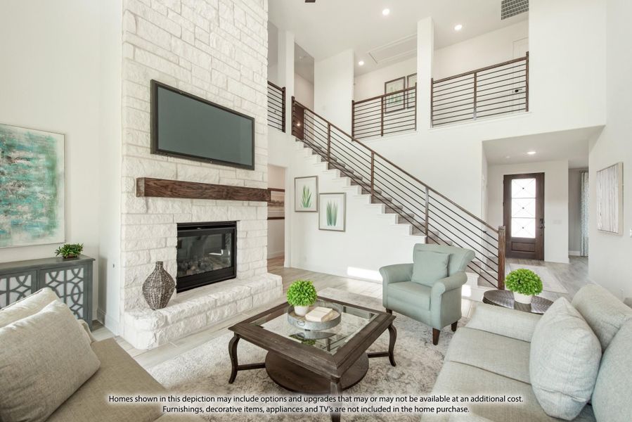Living room with two-story ceiling, stone fireplace, wall-mounted TV, and open staircase with metal railing