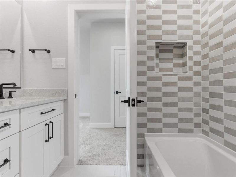 Bathroom featuring a white bathtub, tiled shower surround with a built-in niche, white vanity with black hardware and faucet, and light-toned countertop