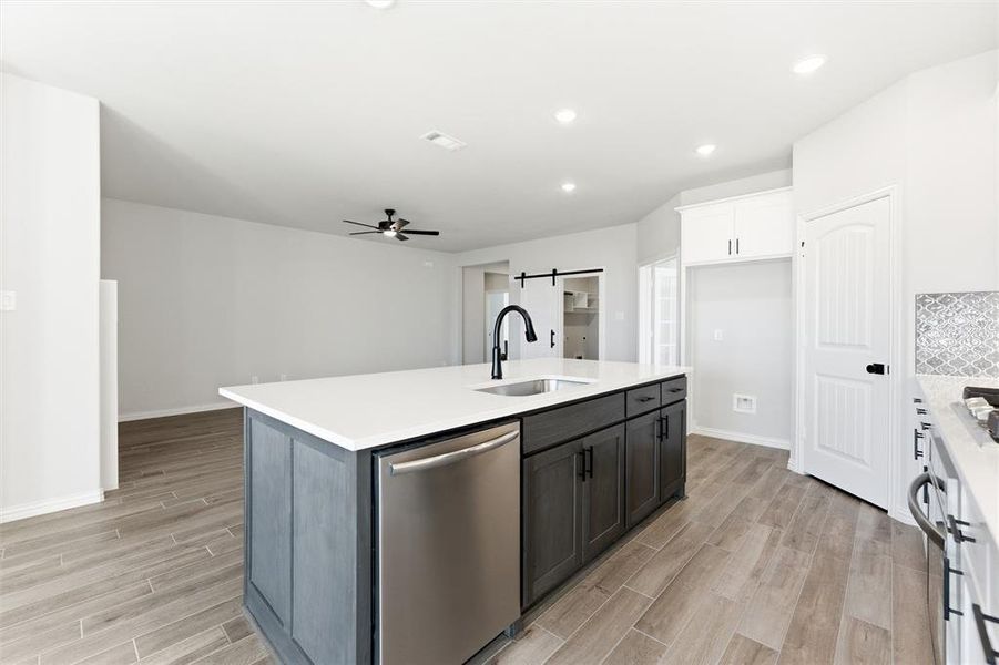 Kitchen with a barn door, dishwasher, wood finish floors, white cabinets, and recessed lighting