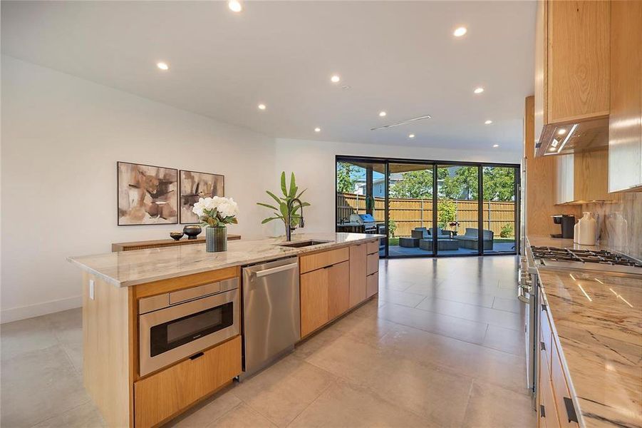 Kitchen with light stone countertops, appliances with stainless steel finishes, light brown cabinets, an island with sink, and sink