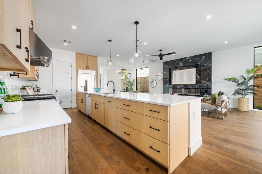 Kitchen featuring built in refrigerator, light brown cabinetry, hardwood / wood-style flooring, a sink, and exhaust hood