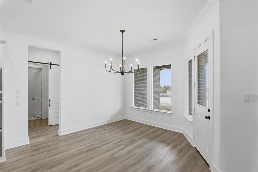 Unfurnished dining area with a barn door, crown molding, a chandelier, and light wood-type flooring