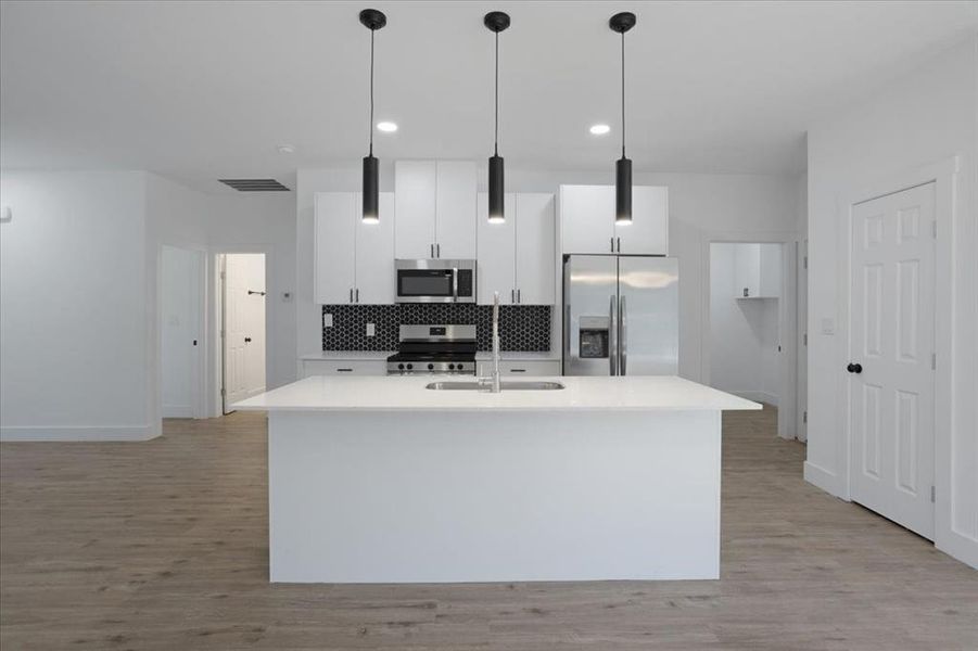 Kitchen with a center island with sink, decorative light fixtures, light hardwood / wood-style floors, white cabinetry, and stainless steel appliances