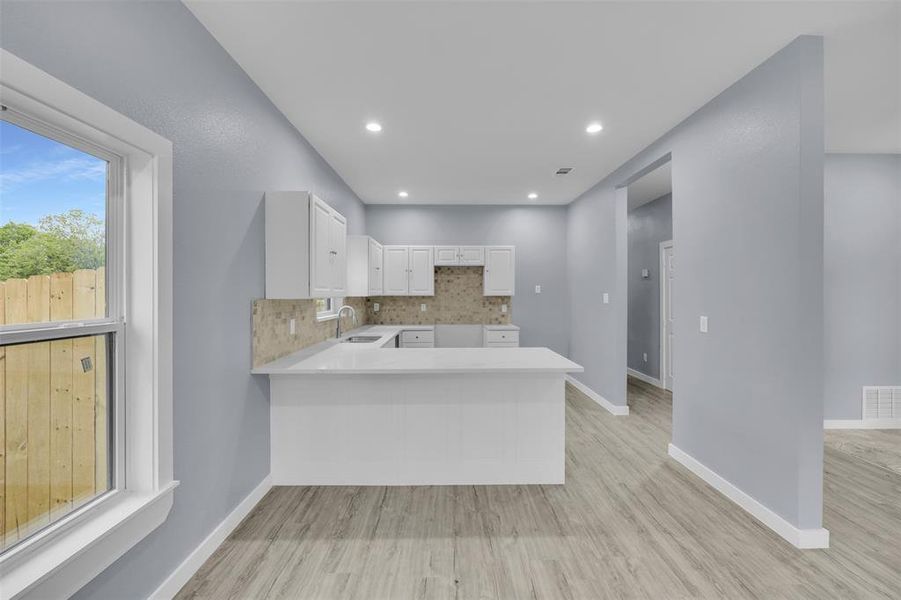 Kitchen featuring light countertops, a peninsula, white cabinets, tasteful backsplash, and light wood-style floors