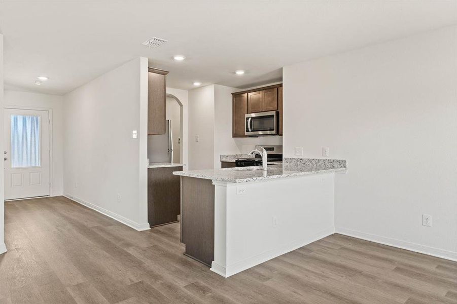 Kitchen featuring stainless steel appliances, light stone counters, light wood-type flooring, and kitchen peninsula