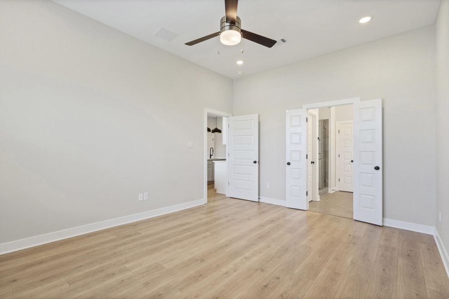 Spacious room featuring wood-finish flooring, light grey walls, and a contemporary ceiling fan with integrated lighting Spacious room featuring wood-finish flooring, light grey walls, and a contemporary ceiling fan with integrated lighting