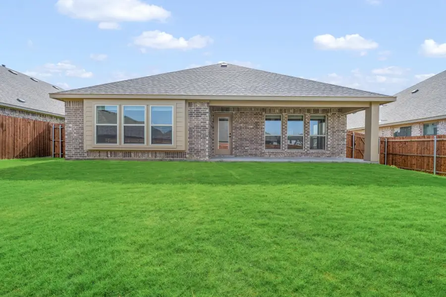 Brick home rear exterior with covered patio, large windows, and fenced green backyard lawn