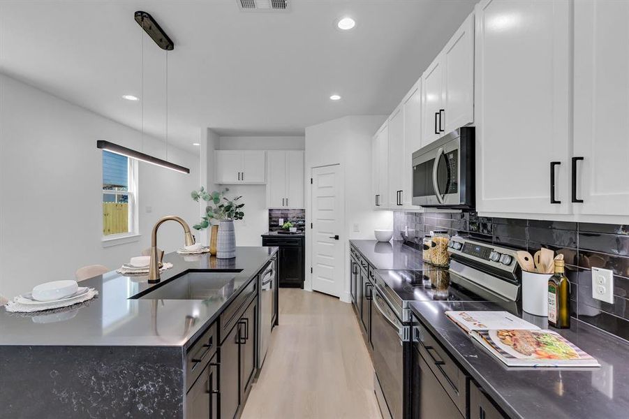 Kitchen with light wood-type flooring, stainless steel appliances, sink, decorative light fixtures, and white cabinets