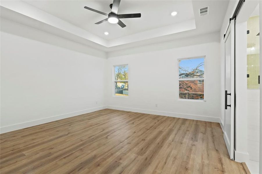 Unfurnished room with a barn door, ceiling fan, recessed lighting, light wood-style floors, and a raised ceiling