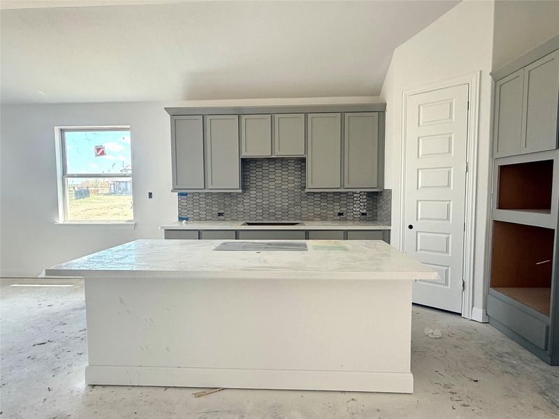 Kitchen featuring concrete floors, a kitchen island, gray cabinets, and decorative backsplash Kitchen featuring concrete floors, a kitchen island, gray cabinets, and decorative backsplash