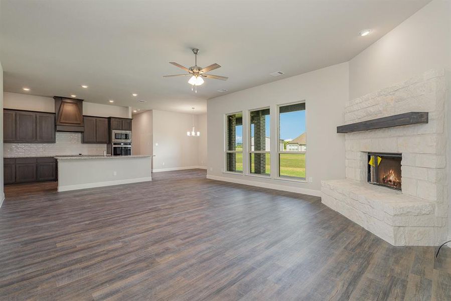 Unfurnished living room featuring ceiling fan with notable chandelier, a fireplace, and dark hardwood / wood-style flooring