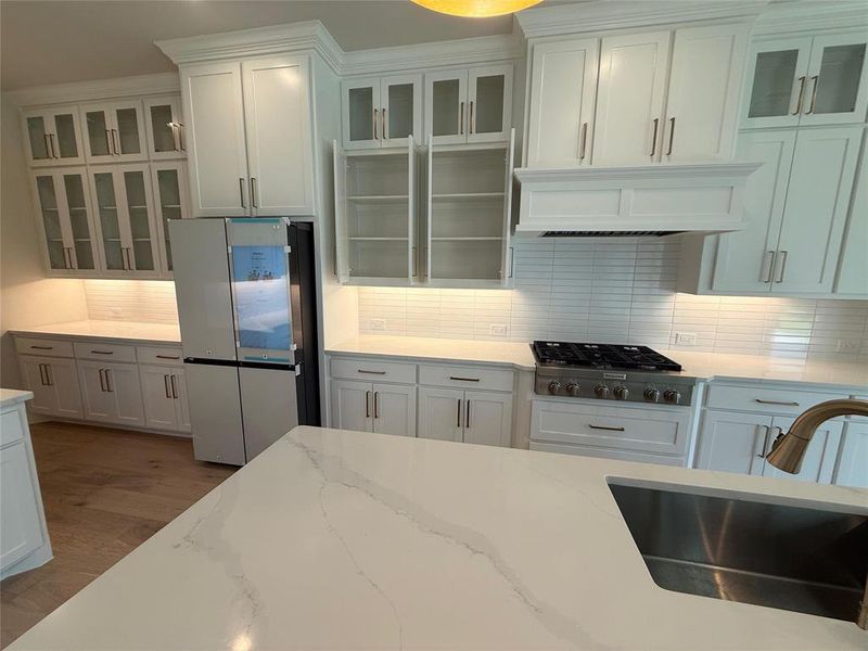 Kitchen featuring glass insert cabinets, backsplash, freestanding refrigerator, and light stone countertops Kitchen featuring glass insert cabinets, backsplash, freestanding refrigerator, and light stone countertops