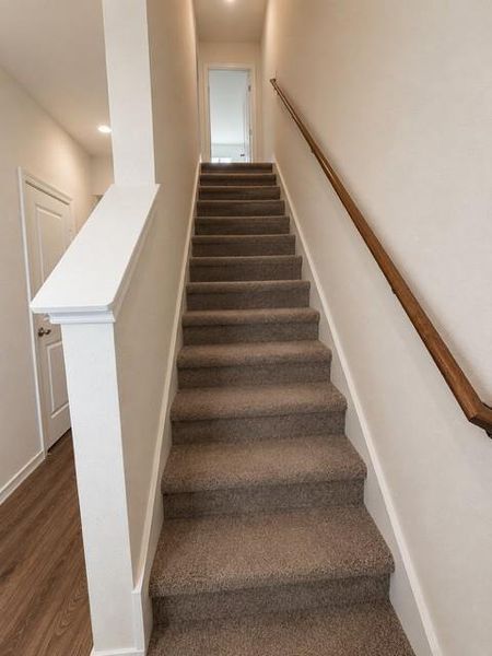Carpeted staircase featuring a natural wood-finish handrail and recessed lighting Carpeted staircase featuring a natural wood-finish handrail and recessed lighting