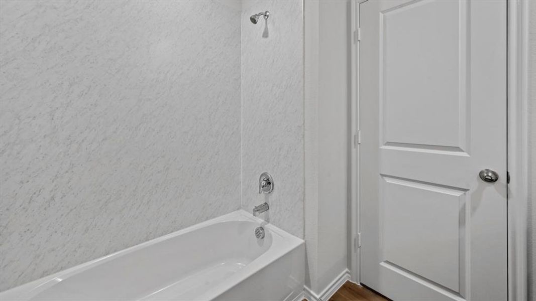 White bathtub with a textured shower surround, chrome fixtures, and a classic paneled interior door