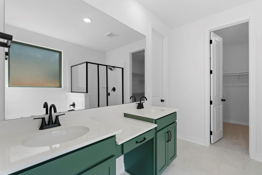 Stylish primary bathroom with green cabinetry, light countertops, and a double sink vanity.