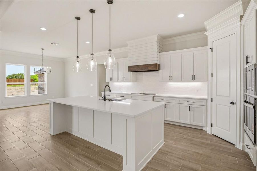 Kitchen with crown molding, an island with sink, white cabinetry, and decorative backsplash