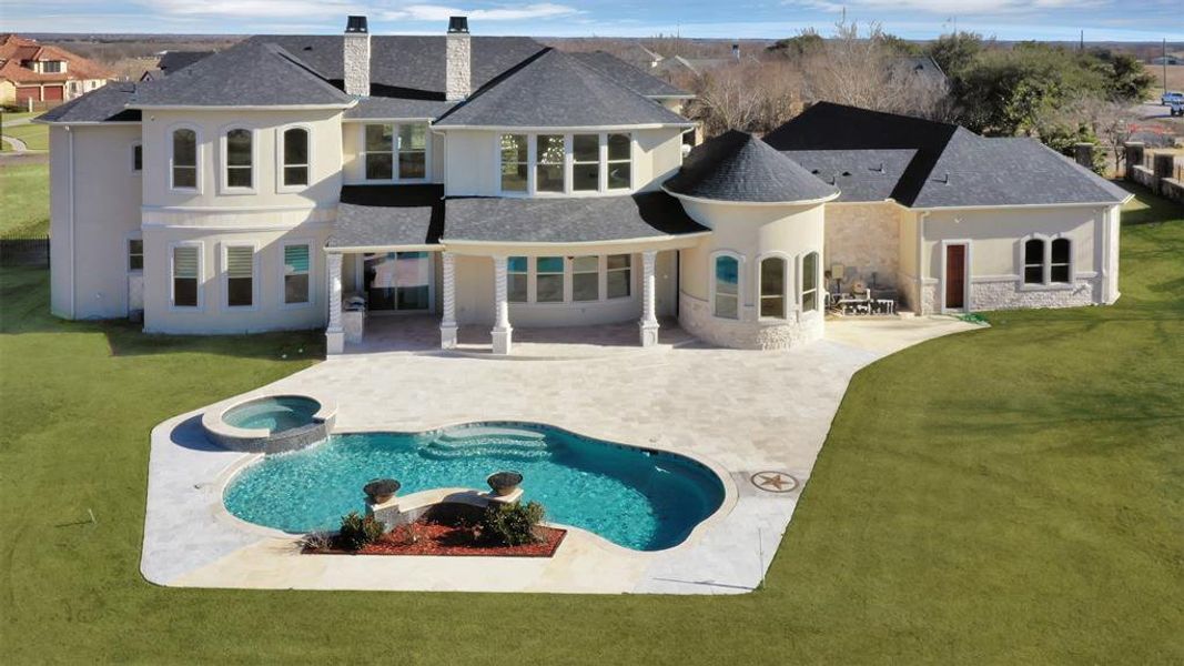 Rear view of property with a swimming pool with hot tub, a patio, and a lawn