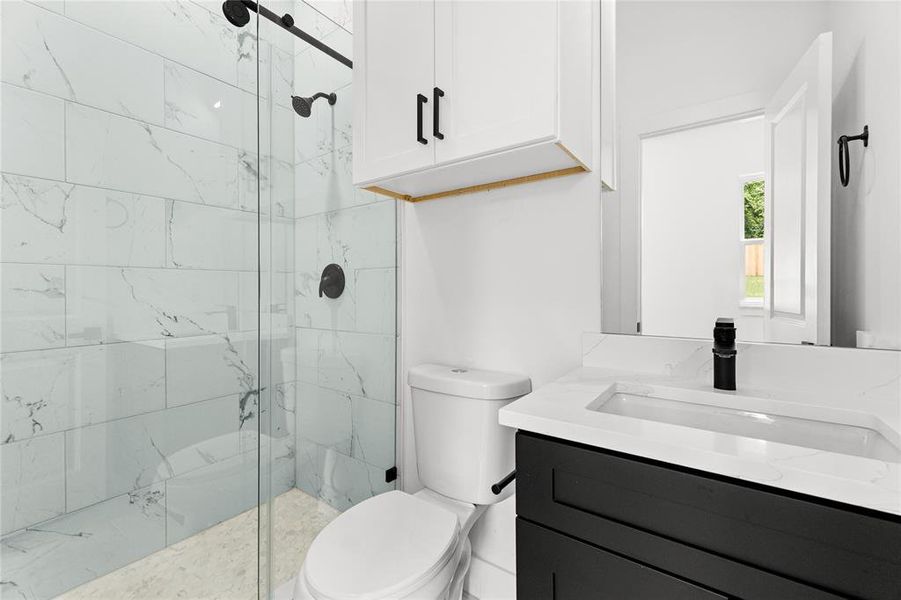 Modern bathroom featuring a glass-enclosed shower with subway-style wall tile, a matte black vanity with an integrated sink, and white upper cabinetry