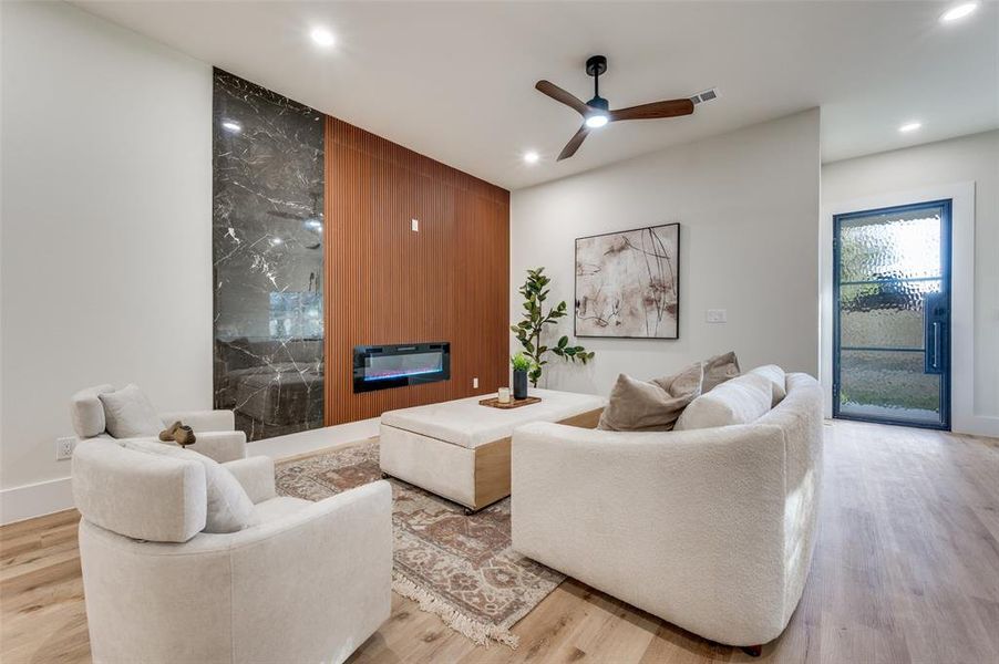 Living area featuring a floor-to-ceiling accent wall with a dark veined slab and wood-finish paneling, an integrated linear fireplace, and recessed lighting