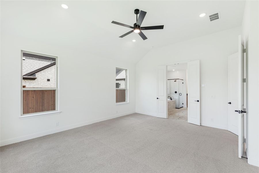 Spacious bedroom with vaulted ceiling, ceiling fan, carpet flooring, and open door to ensuite bathroom