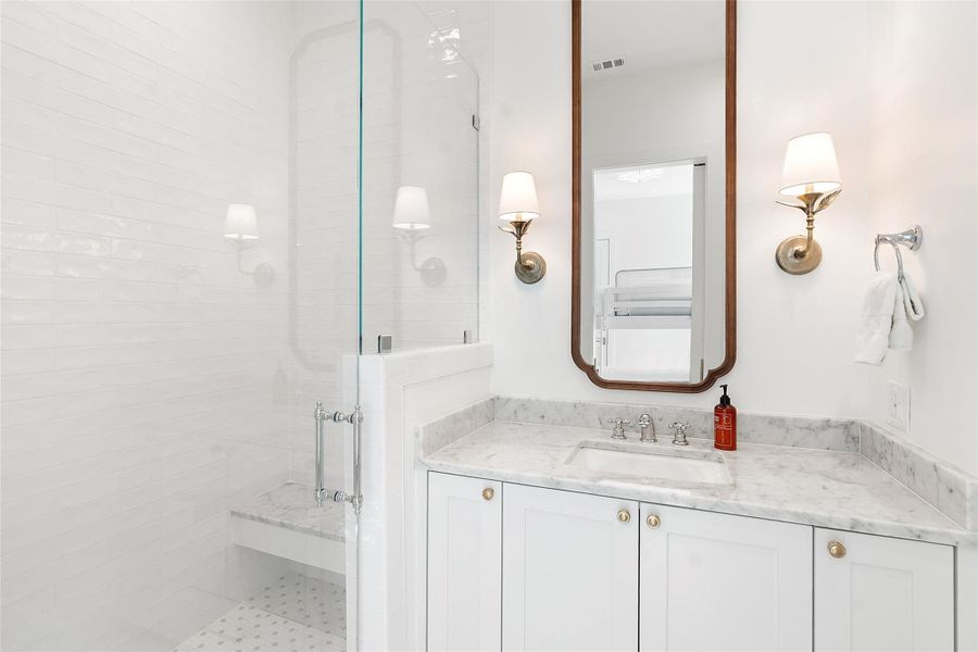 White subway tile adorns the shower with a built-in bench, complementing the marble-topped vanity. White subway tile adorns the shower with a built-in bench, complementing the marble-topped vanity.