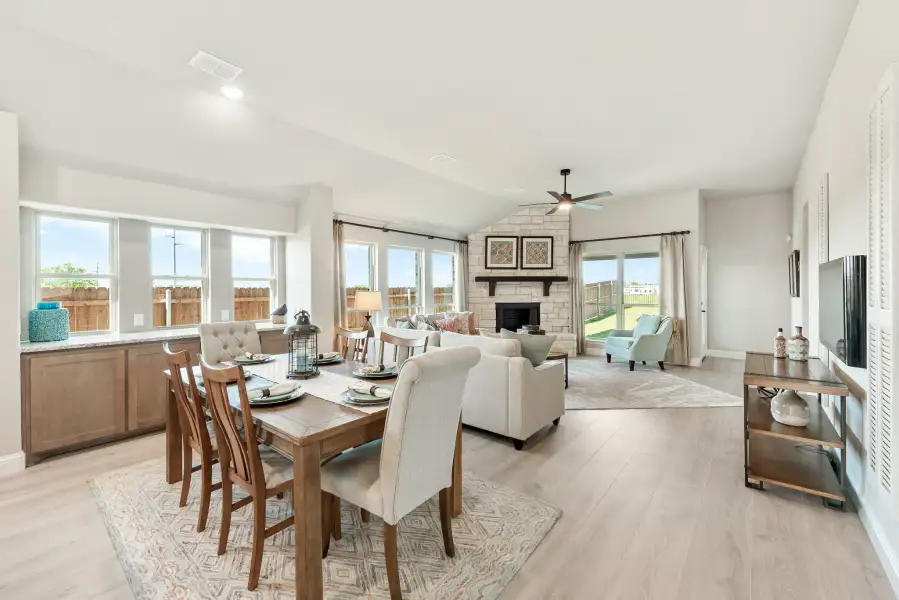Open-concept dining and living area with stone fireplace, ceiling fan, and light wood floors Open-concept dining and living area with stone fireplace, ceiling fan, and light wood floors