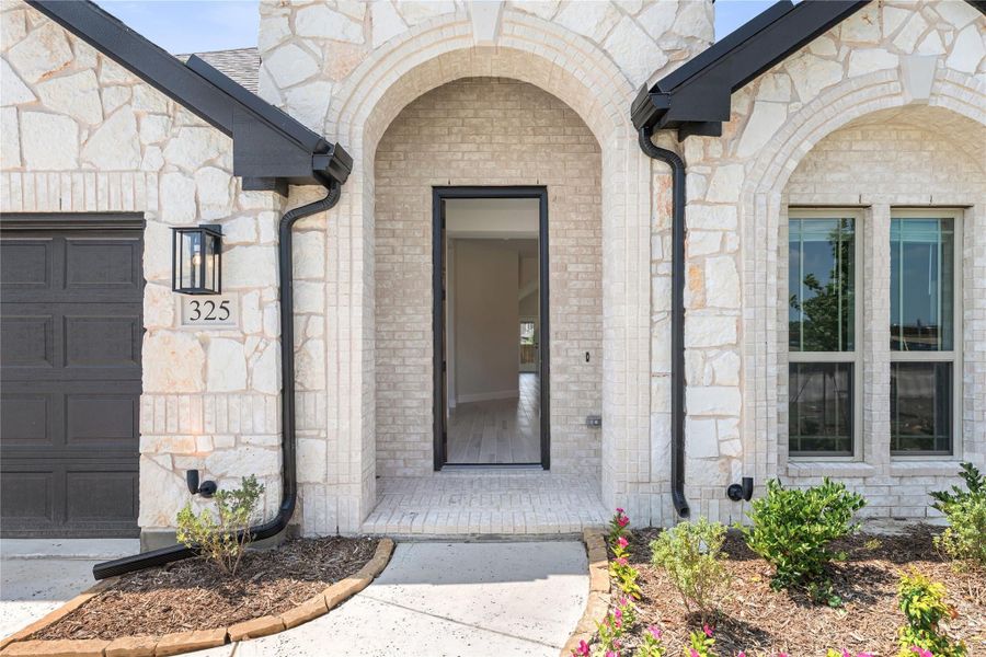 Stone home entrance with arched doorway, black front door, and address number 325 on the exterior wall.