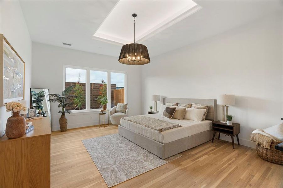 Bedroom featuring light wood finished floors, a raised ceiling, and hanging lights Bedroom featuring light wood finished floors, a raised ceiling, and hanging lights