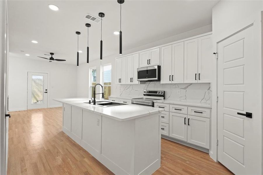 Kitchen with white cabinetry, sink, stainless steel appliances, and an island with sink