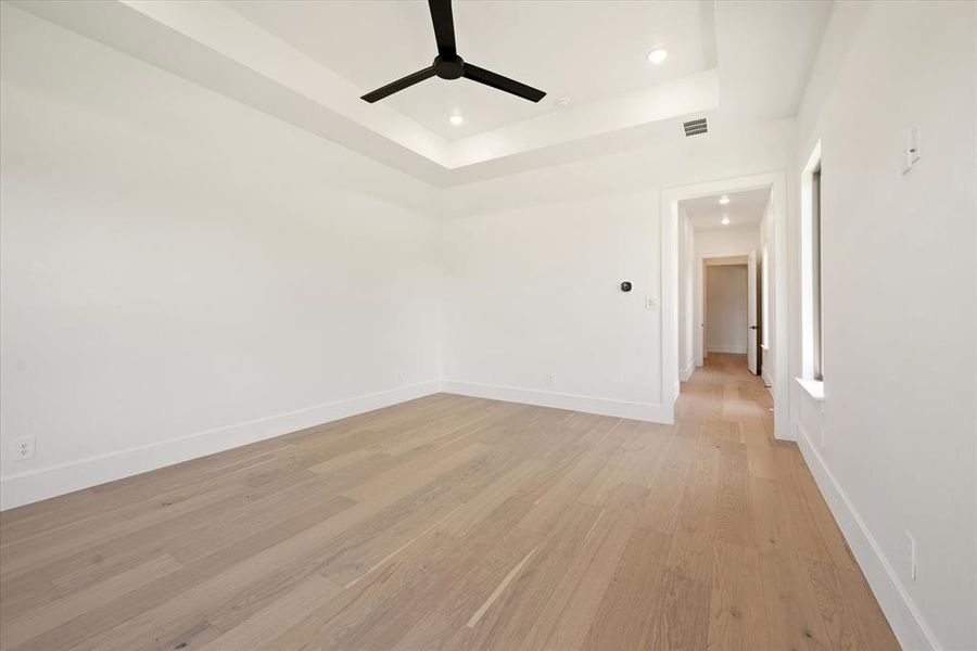 Unfurnished room with ceiling fan, light wood-type flooring, and a tray ceiling