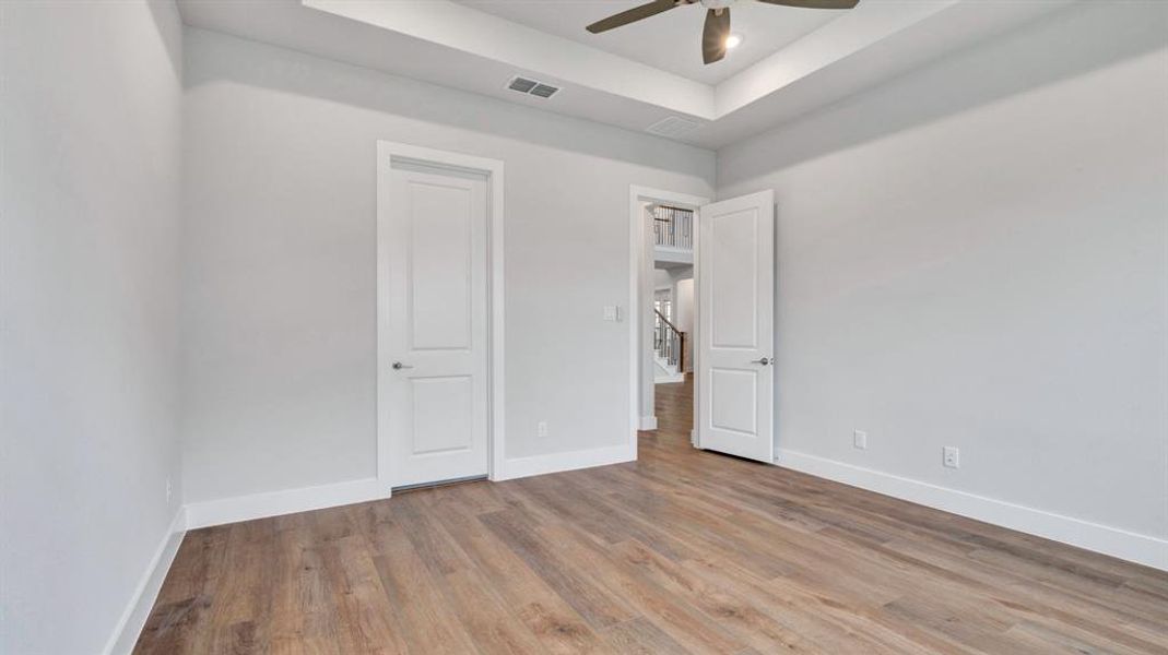 Unfurnished bedroom with a tray ceiling, ceiling fan, and light wood-type flooring