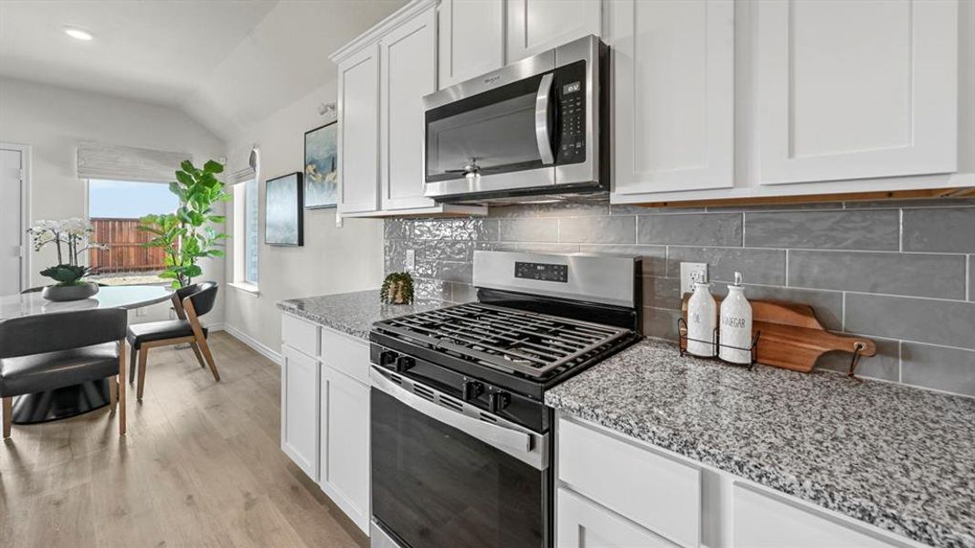 Kitchen featuring stainless steel appliances, white cabinetry, light stone counters, light wood-style flooring, and lofted ceiling