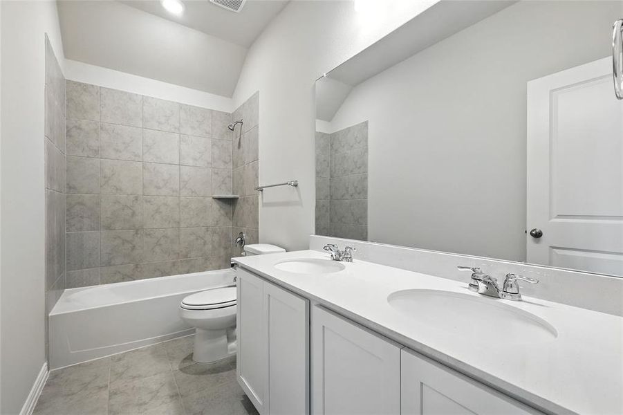 Full bathroom featuring double vanity,  shower combination, vaulted ceiling, and light tile patterned flooring