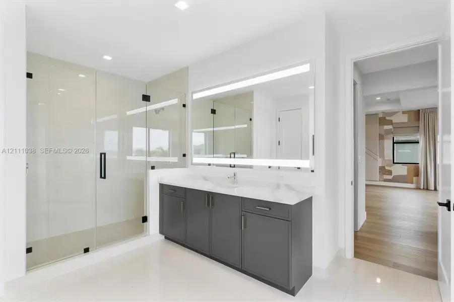 Bathroom featuring a glass-enclosed walk-in shower with tile flooring, a charcoal gray vanity with a stone-finish countertop, and a large integrated LED-lighted mirror